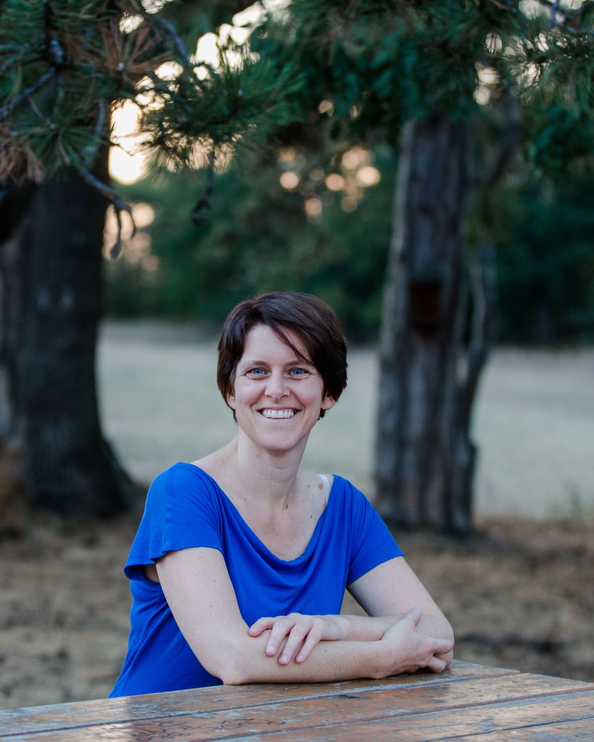 Portrait im Grünen Lächelnde Frau im blauen Shirt lehnt an einem Holztisch im Park