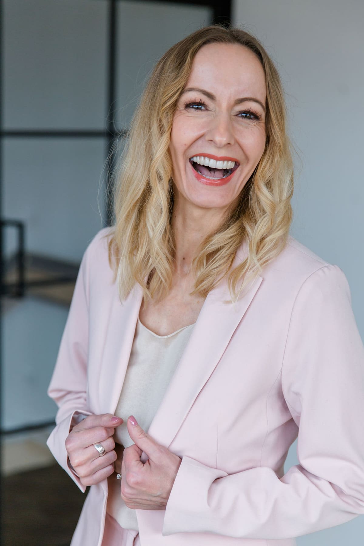Blonde Frau im rosa Blazer lacht offen in die Kamera