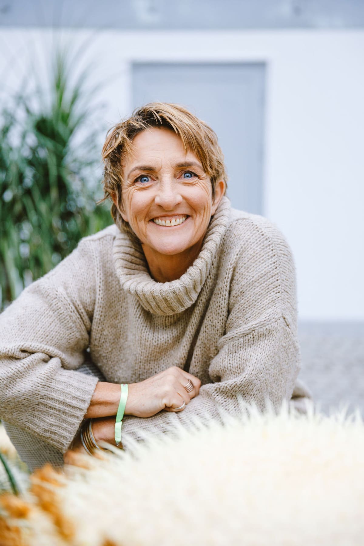 Frau mit kurzen Haaren im Strickpullover lehnt lachend an einem Geländer