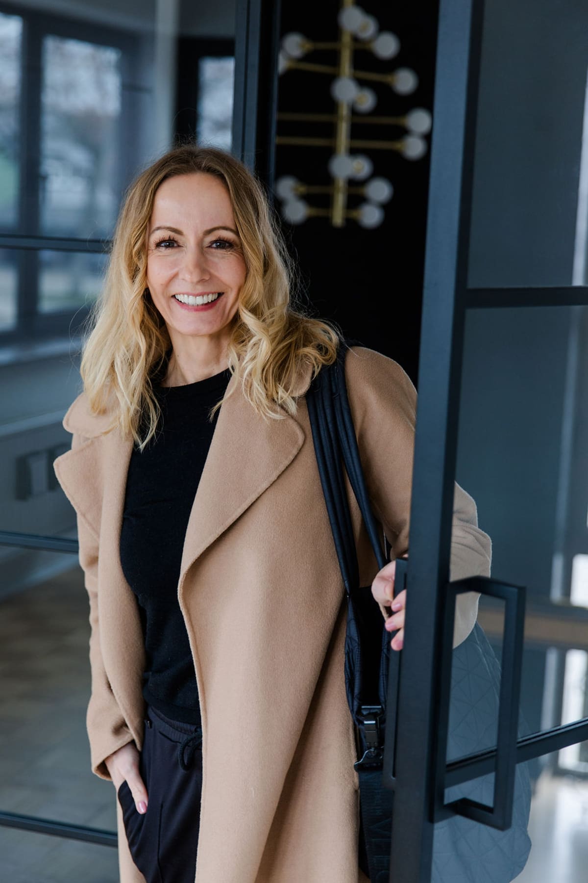 Blonde Frau im Trenchcoat steht in einer Türöffnung