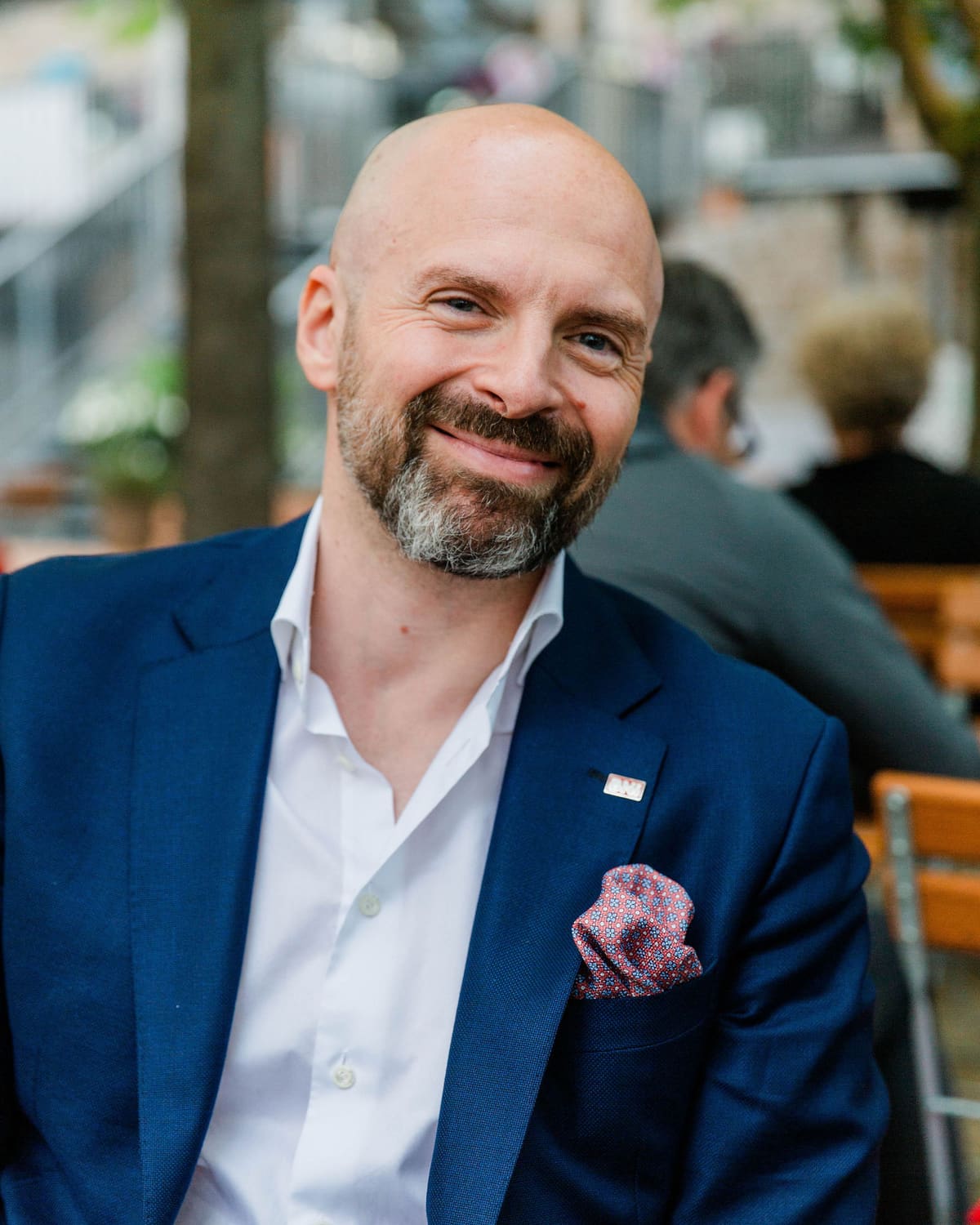 Business-Portrait im Lokal Mann mit Glatze und Bart im dunkelblauen Sakko lächelt in einem Lokal