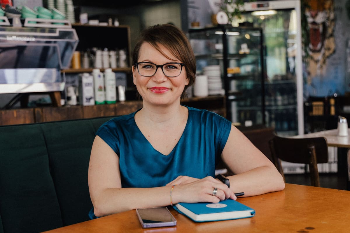 Frau mit Brille sitzt mit Notizbuch an einem Tisch in einem Lokal