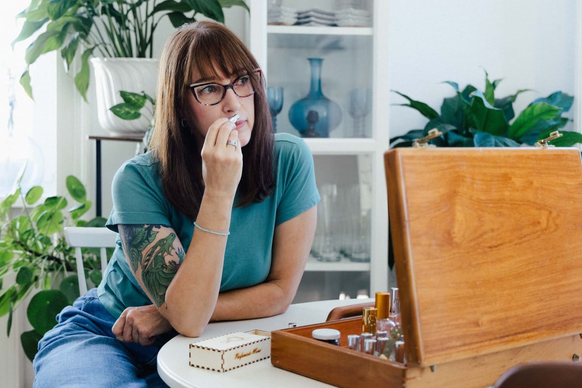 Frau mit Brille sitzt nachdenklich an einem Schreibtisch mit Pflanzen
