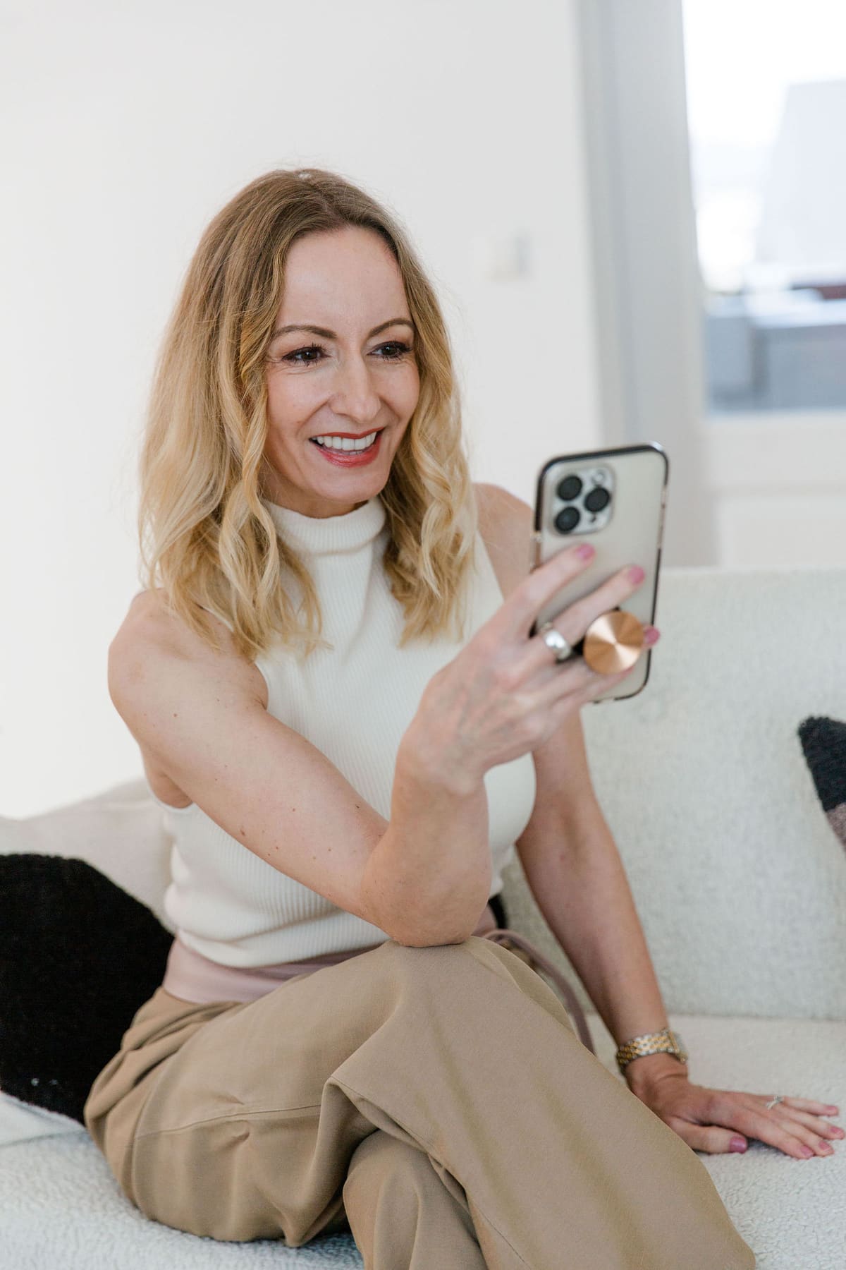 Frau sitzt lächelnd auf dem Sofa und fotografiert mit dem Smartphone