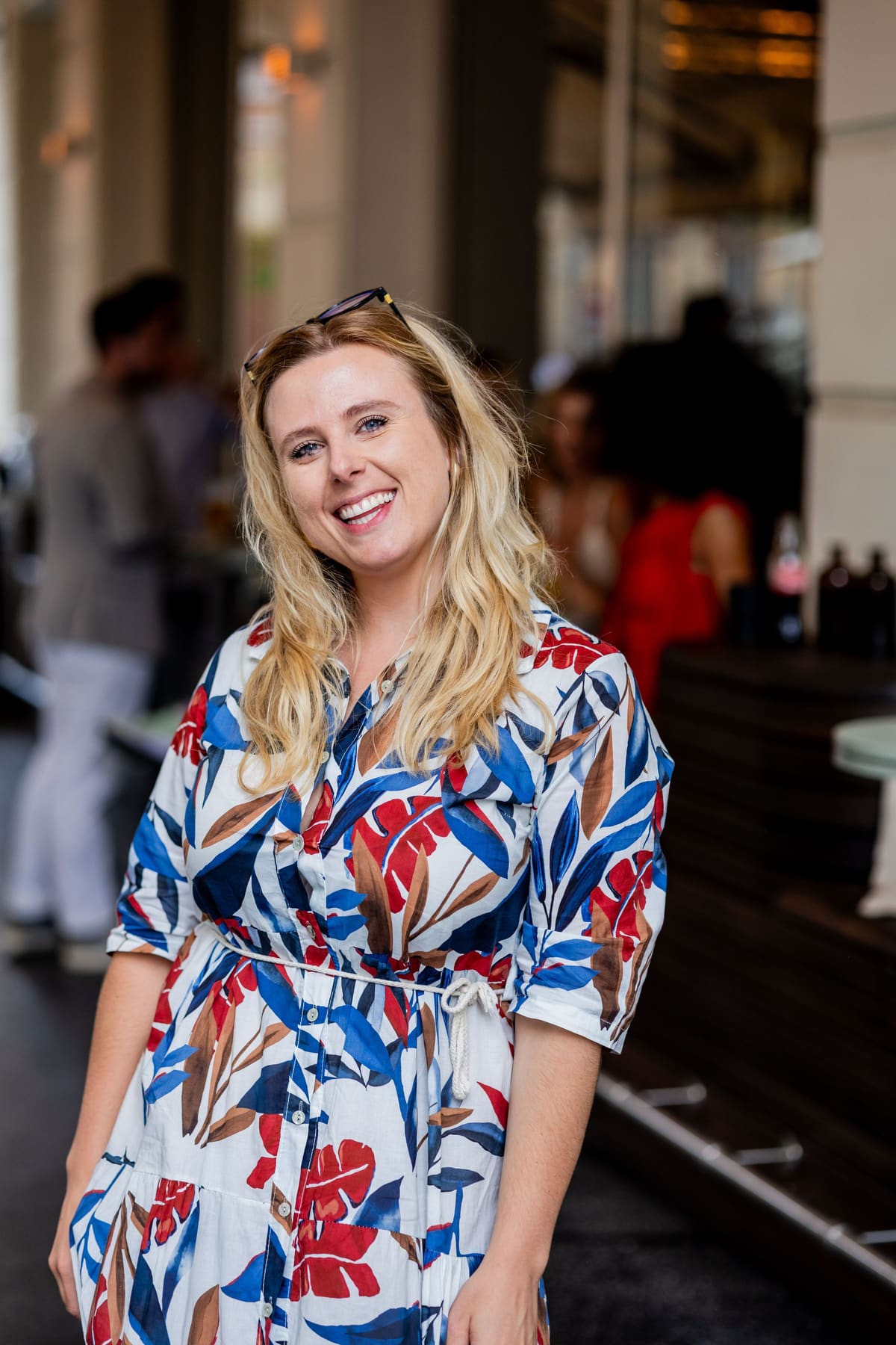 Blonde Frau im bunten Blumenkleid lacht in einem Café