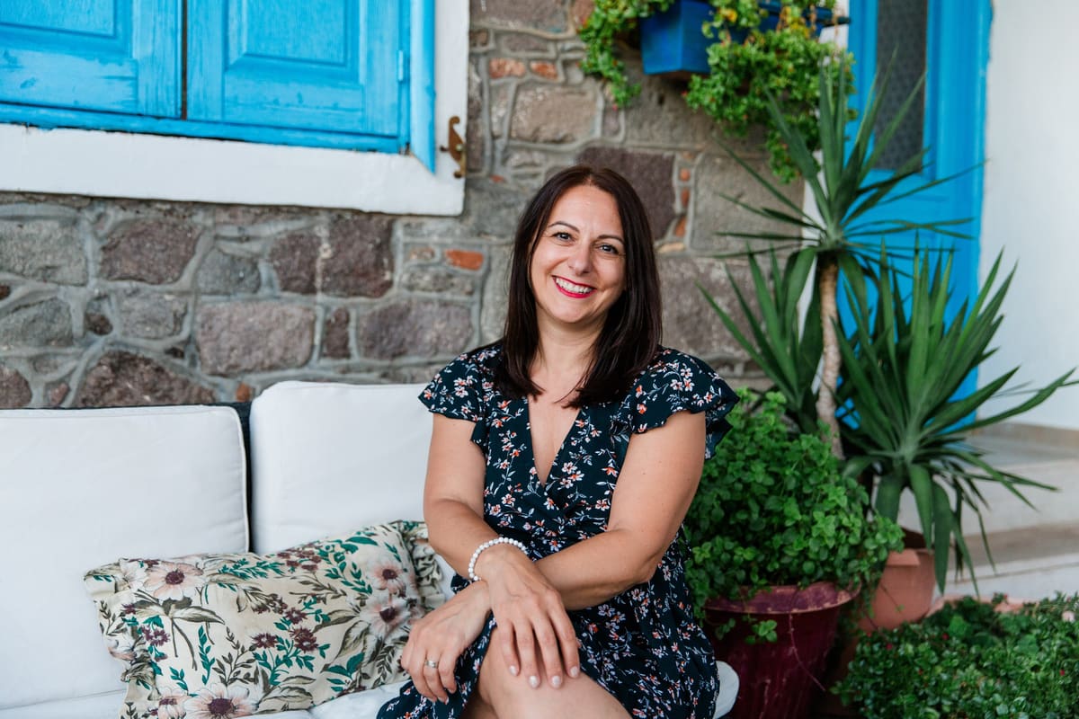 Frau im Blumenkleid sitzt auf einer Terrasse zwischen Pflanzen