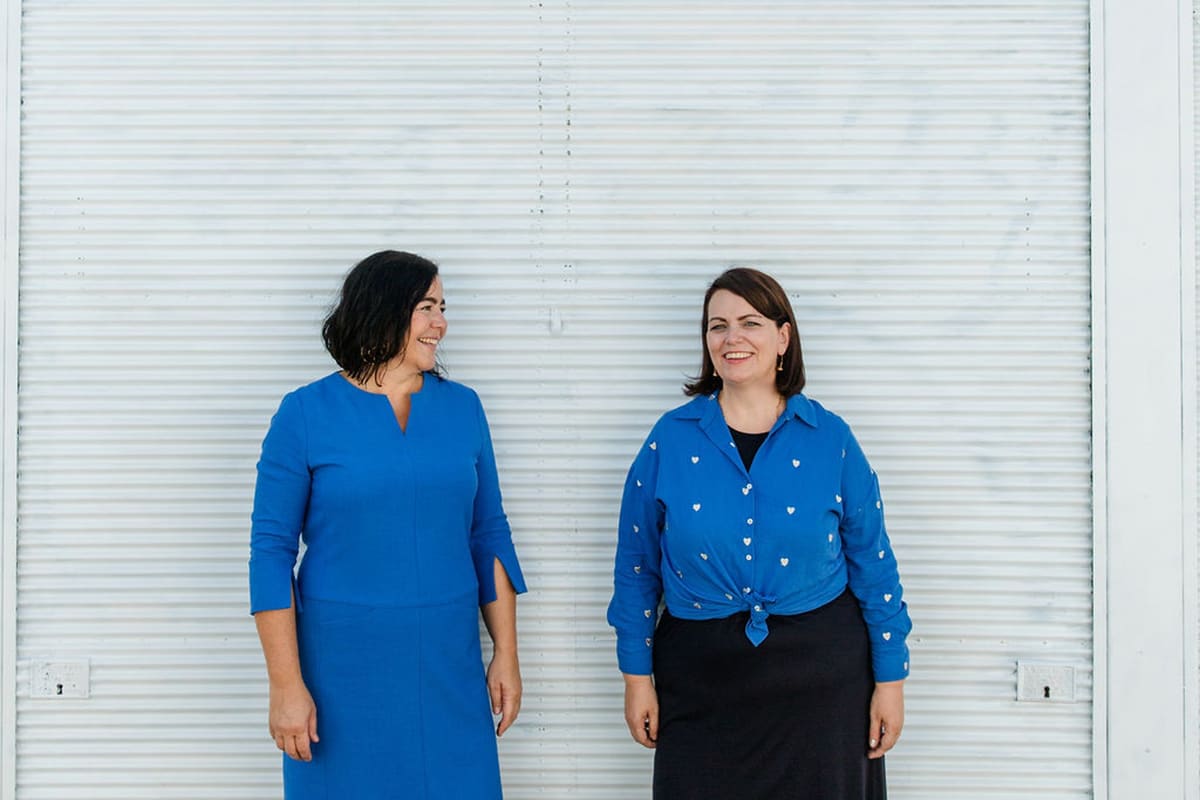 Zwei Frauen in blauen Kleidern stehen vor einer weißen Wand